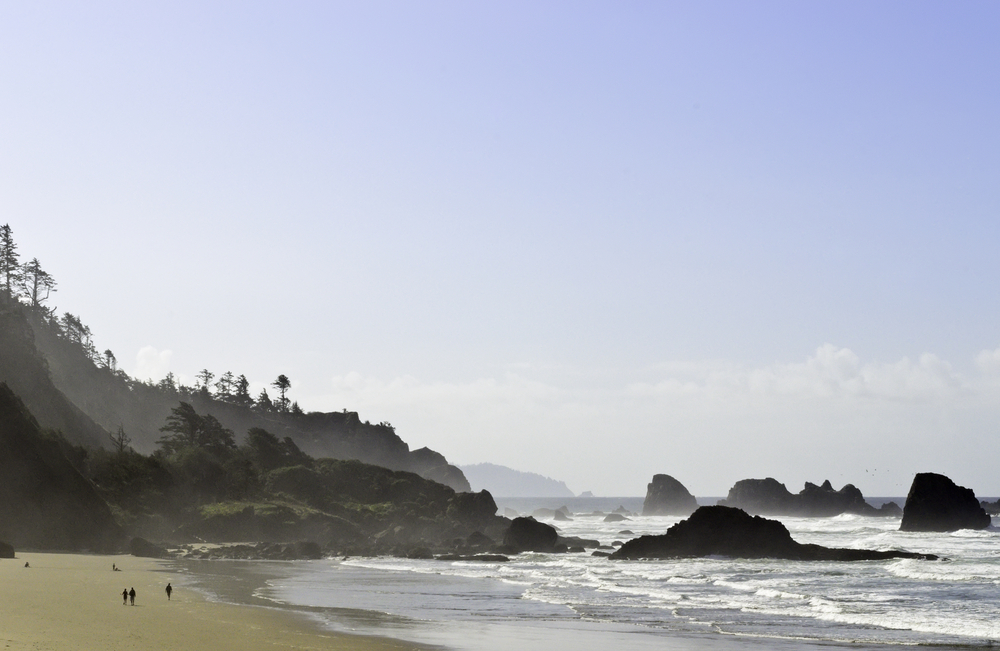 Sandy beach with unidentifiable walkers in the morning along Pacific coastline with sea stacks at Ecola Beach State Park, Cannon Beach, Oregon, USA